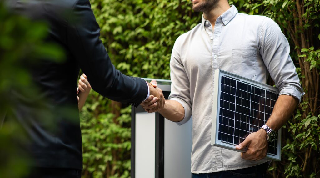 2 Männer schütteln die Hand, einer mit Solarpanel